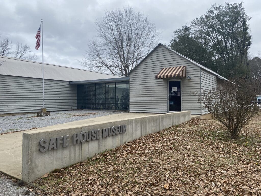 View of small house, now a museum. Sign in front reads "Safe House Museum". American flag flying. Located in Greensboro, AL.