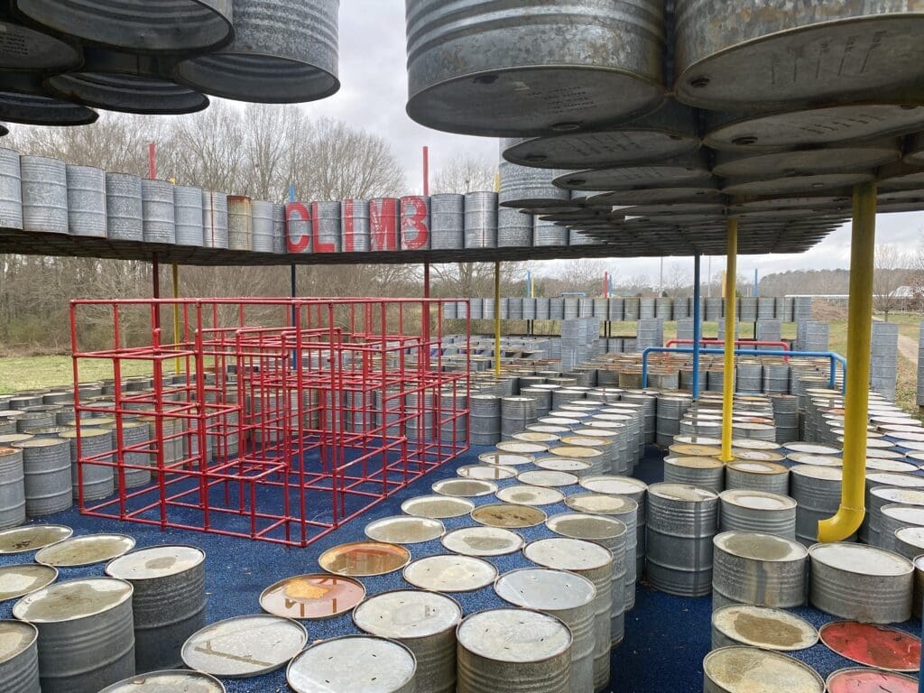 Playground at Lions Park made with 55-gallon oil drums, featuring red bars in the middle for climbing. Located in Greensboro, AL.