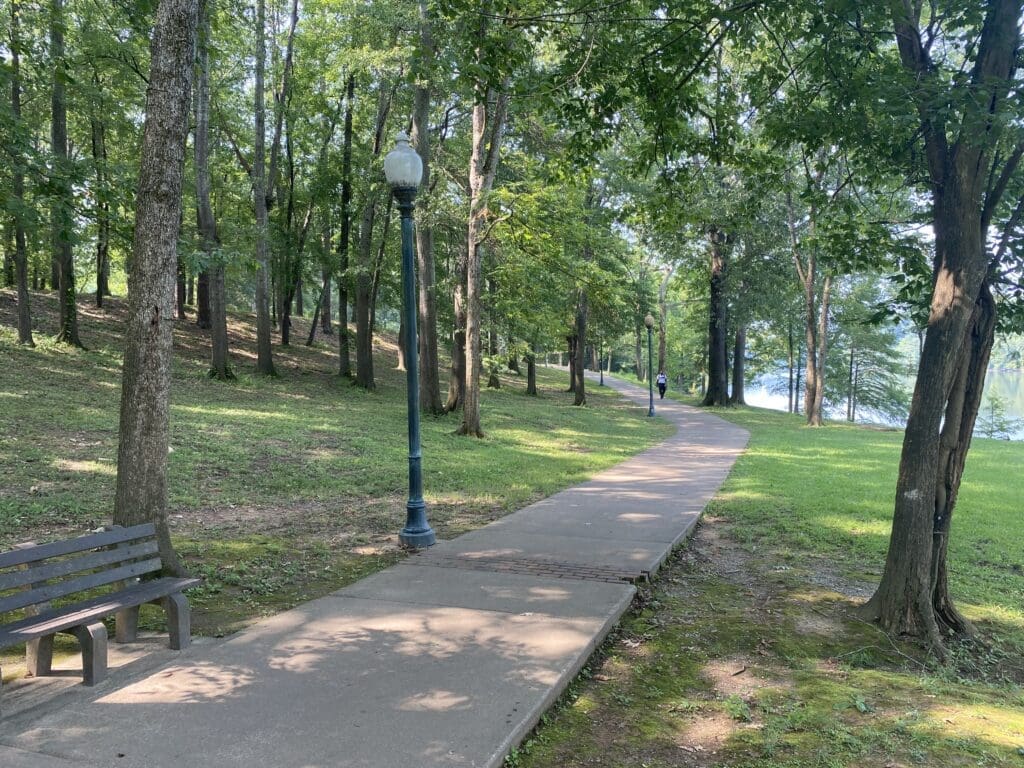 Sidewalk running through a tree-shaded riverside park.