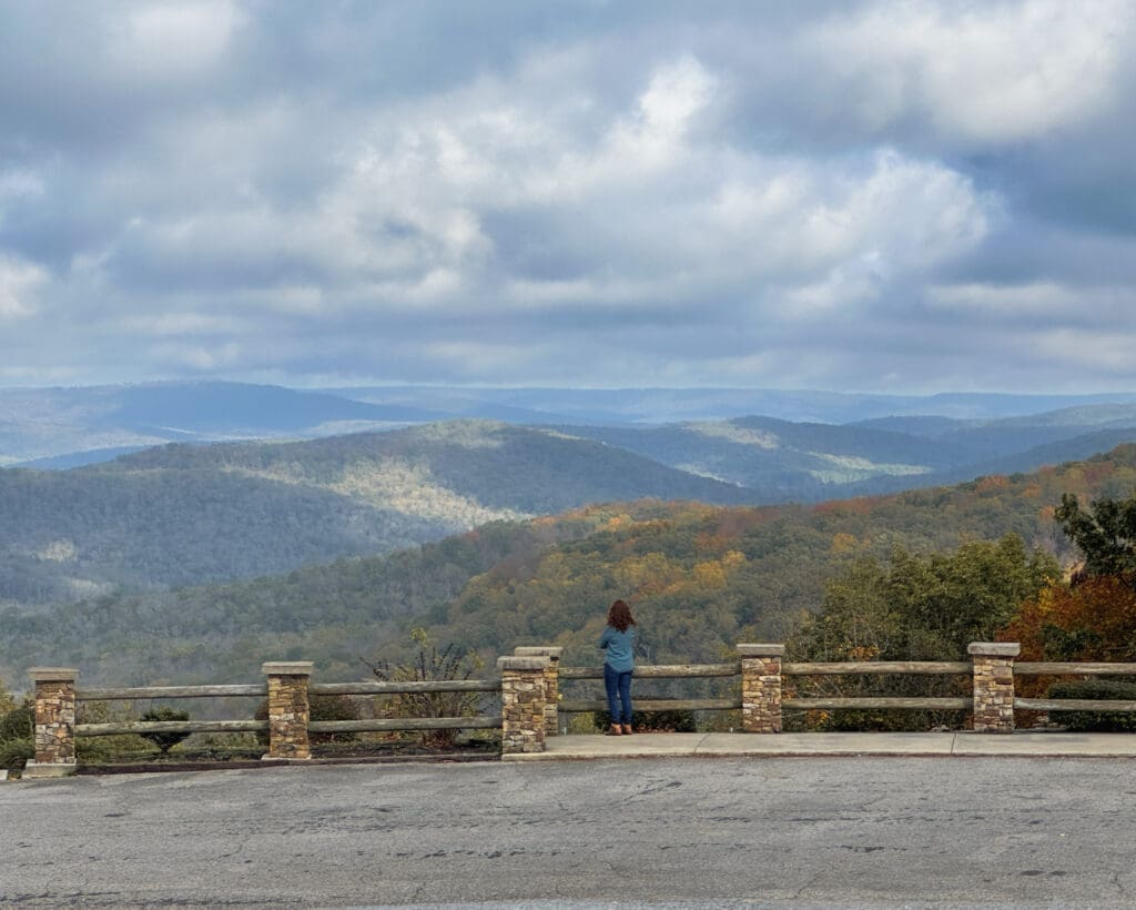 A woman standing at a roadside railing and overlooking southern Appalachian mountains in the fall.