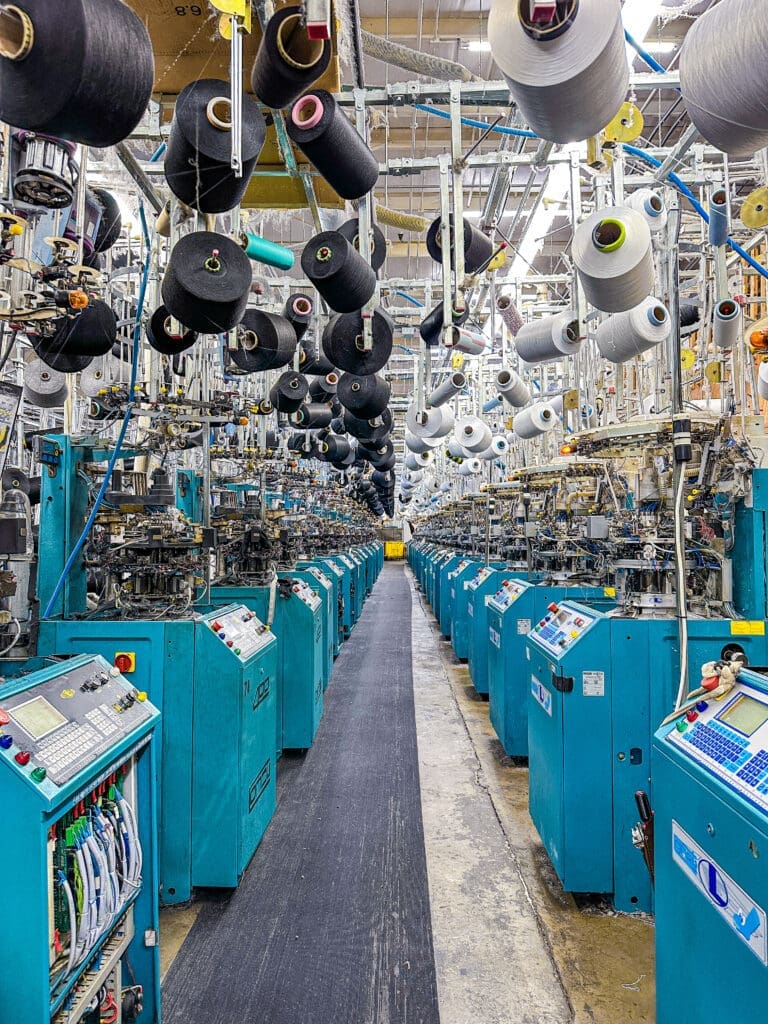 The view looking down a line of sock knitting machines with unused yarn above head height.