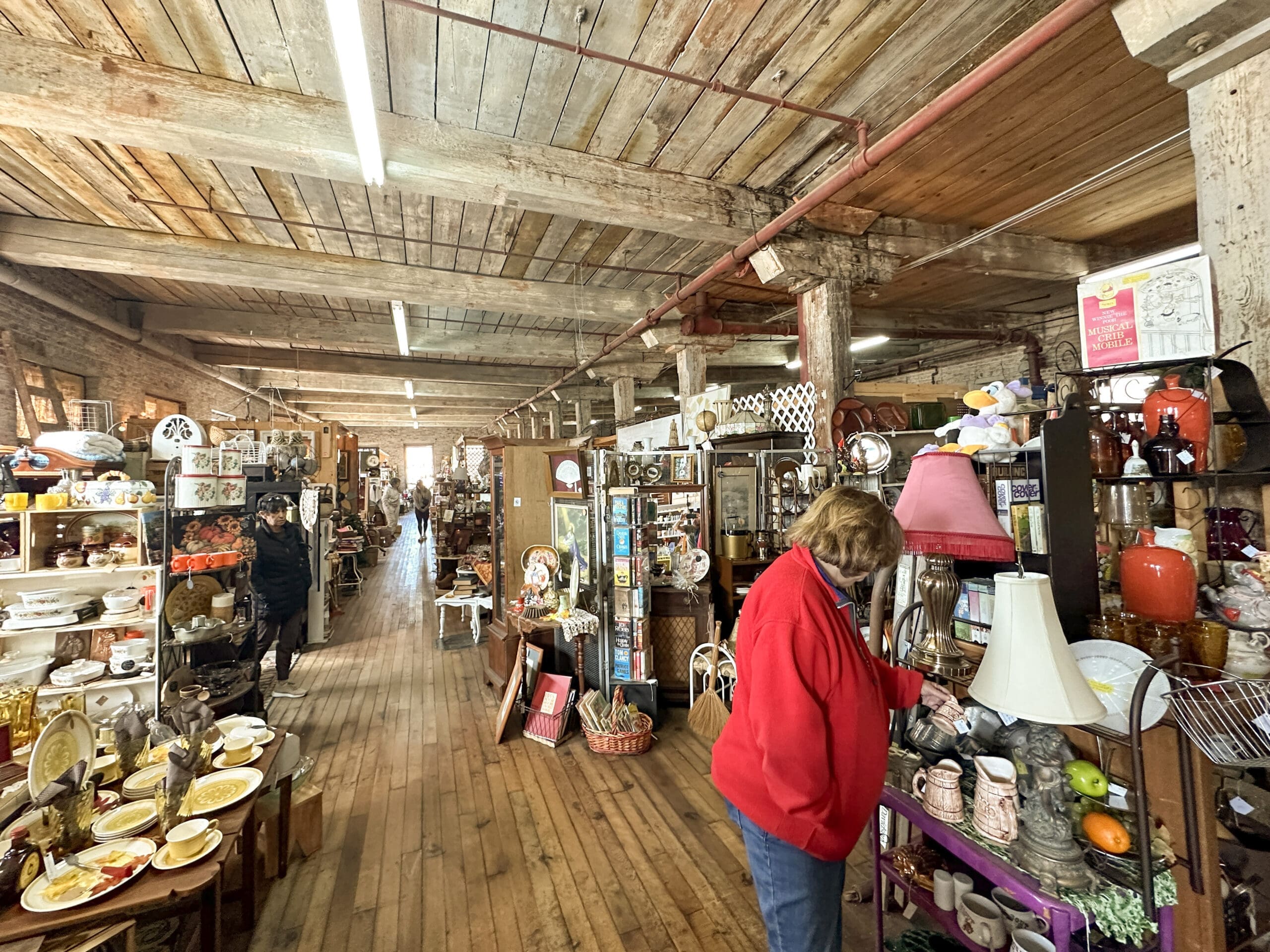 Photo inside an enormous antique mall with wood floors and ceiling. Several people are shopping.
