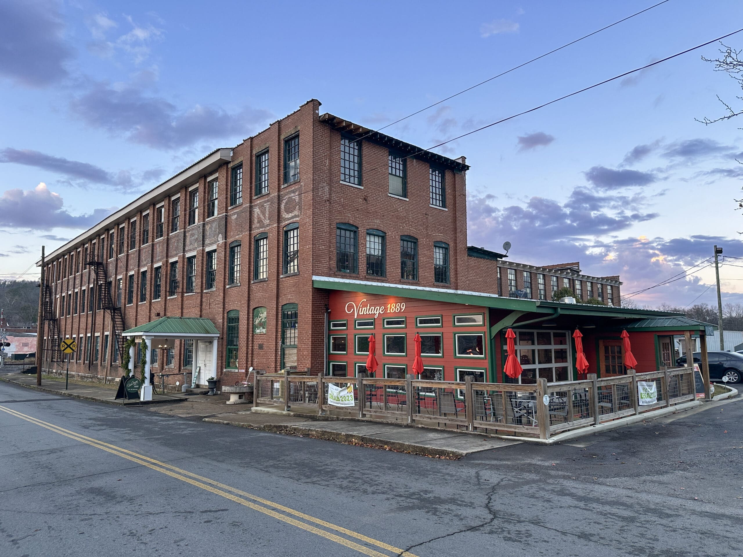 Sunset photo of a large, retired brick textile mill with an attached one-story red restaurant with a sign reading "Vintage 1889".
