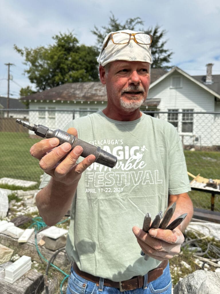 A man (Craigger Browne) with a bandana on his head holds up an automatic tool for carving marble.