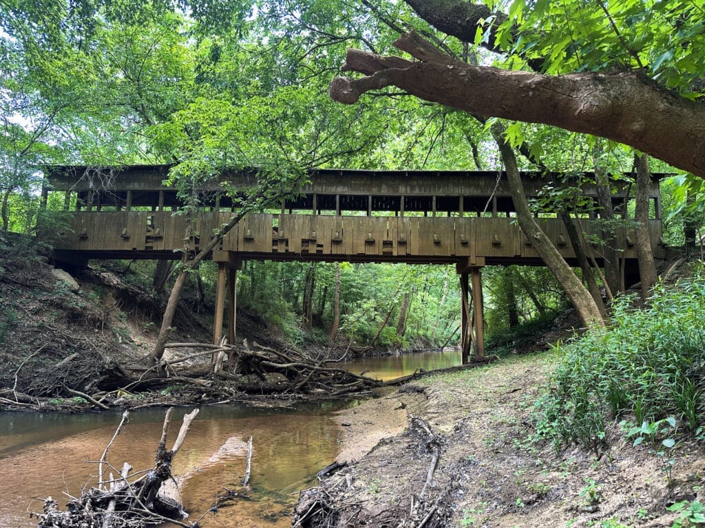 A covered bridge extends through the woods across a creek about 10-feet below.