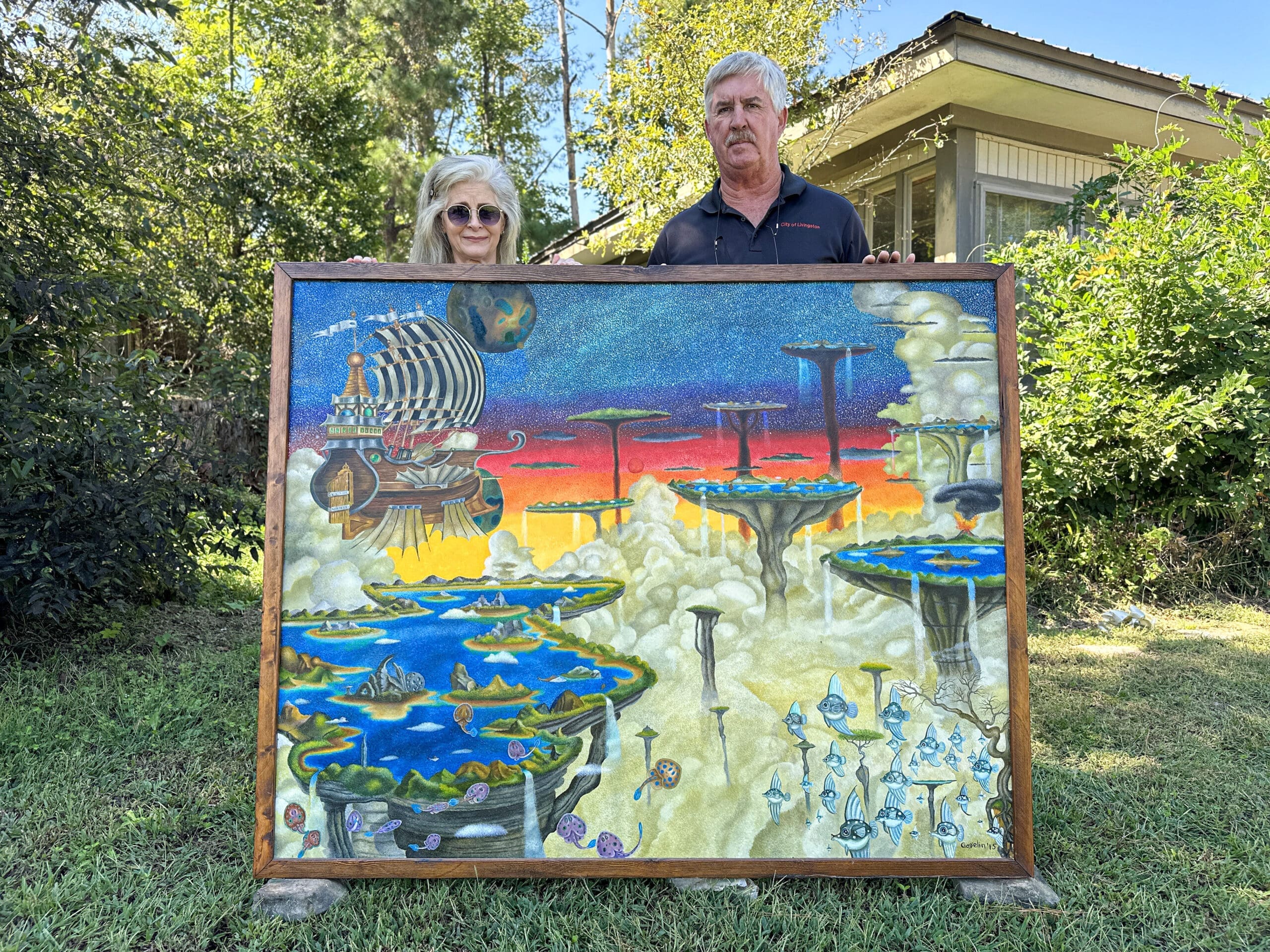 A man and a woman hold up a large, psychedelic painting featuring various sky islands overflowing with water, flying fish, and a large winged flying ship (among other details).