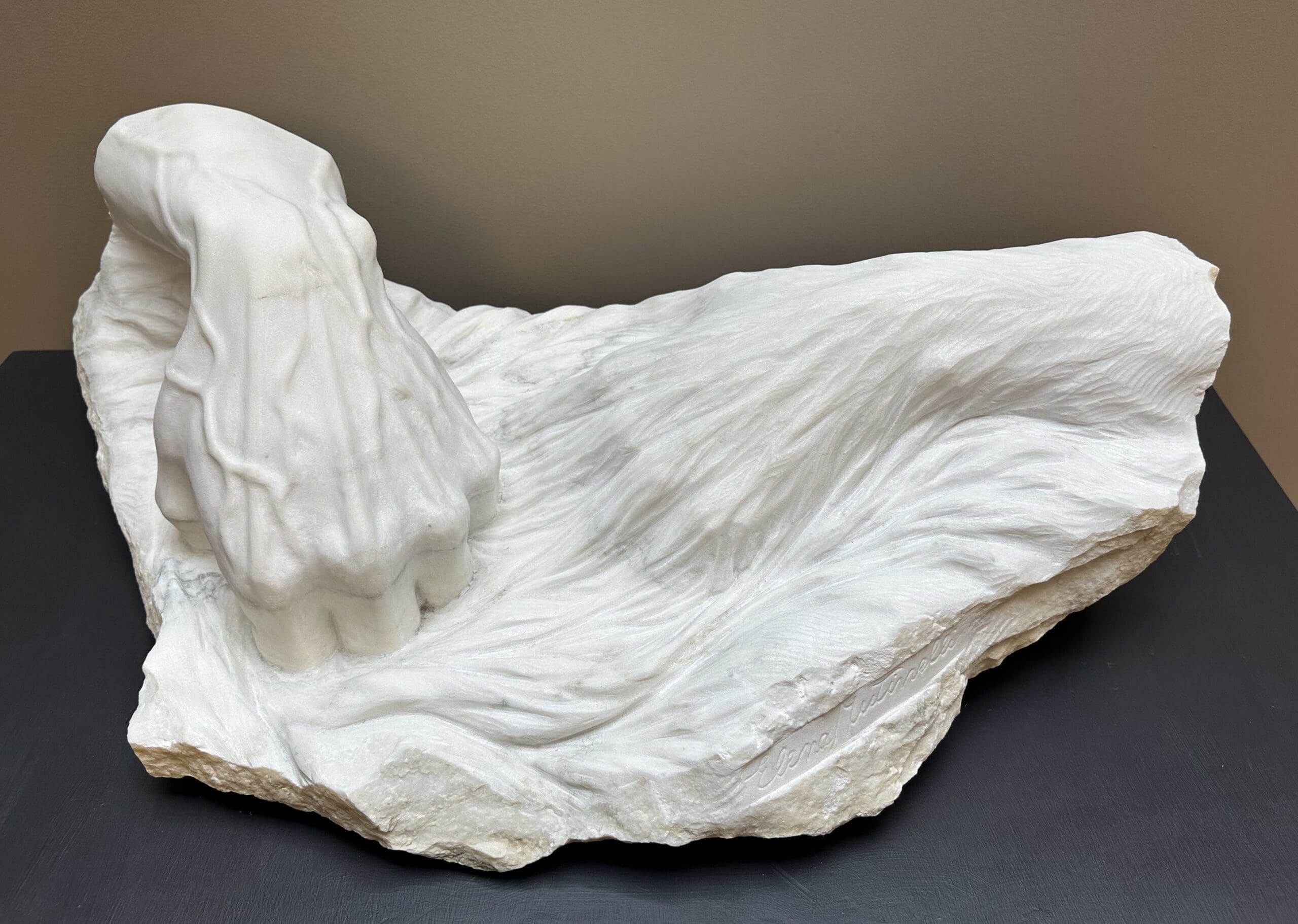 Marble sculpture of two hands, appearing as if intermixed with a water-like material. One hand entering the water, one slightly beneath. Title: “Allora e Ora” (Then and Now) by Elena Mutinelli